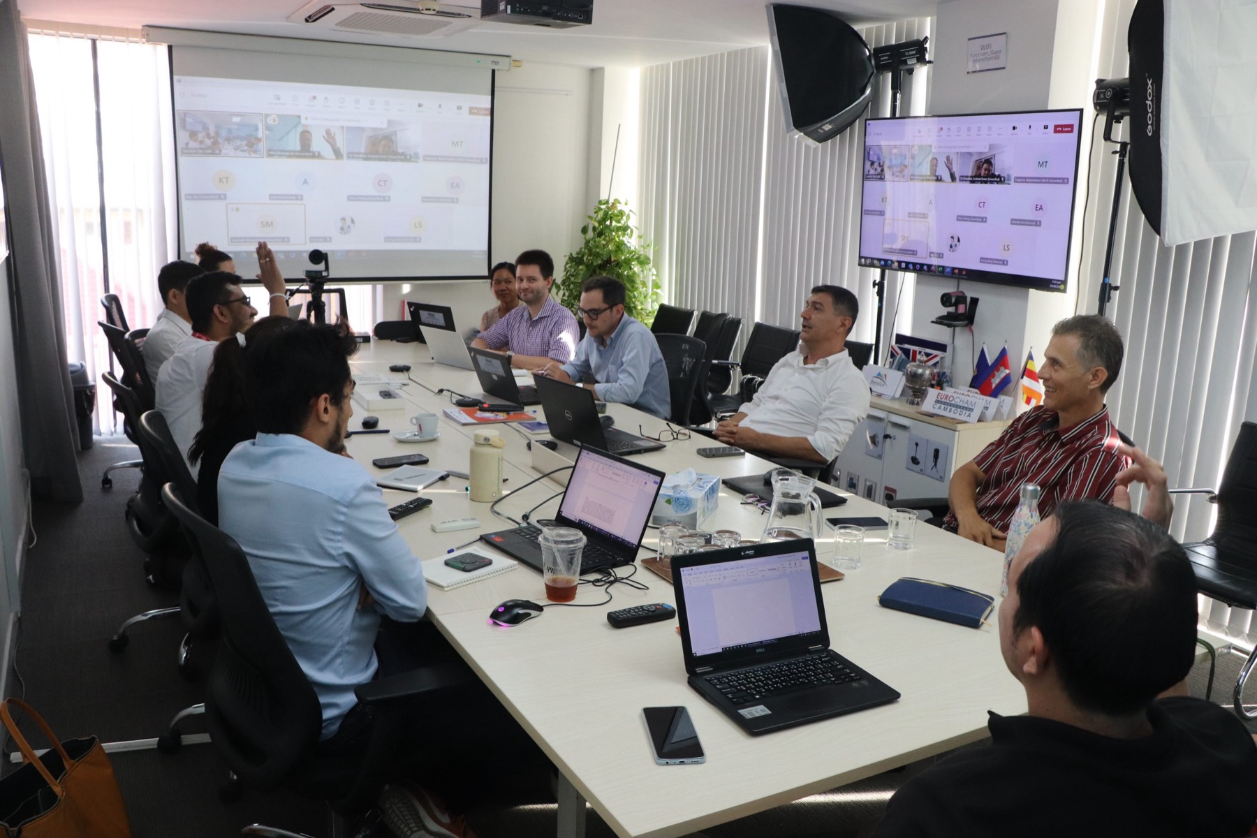 A hybrid committee meeting around the table in the EuroCham Cambodia boardroom, with the remote room on two screens